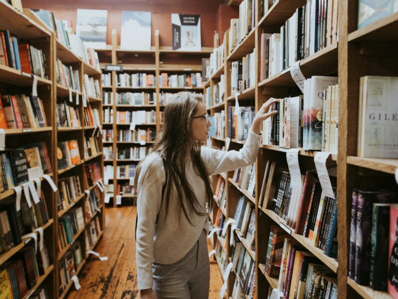 woman holding book on bookshelves