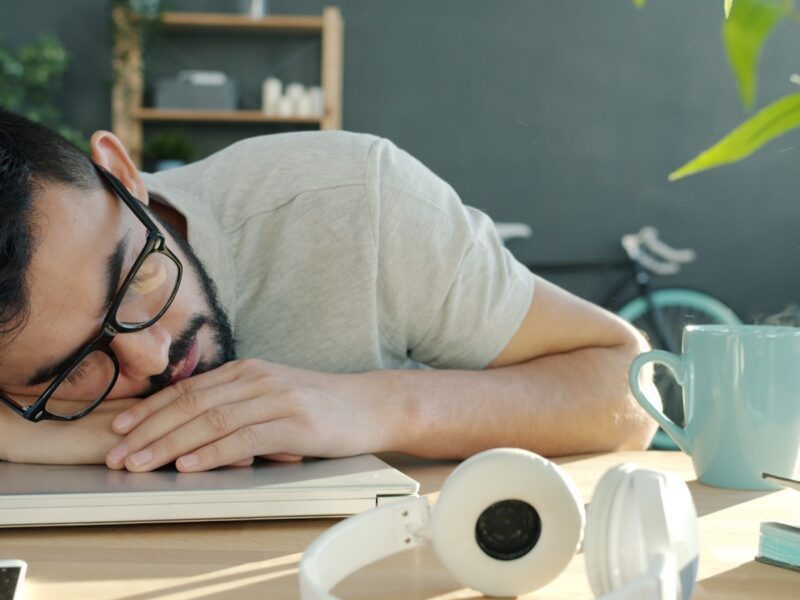 Man sleeping at desk with headphones and coffee.